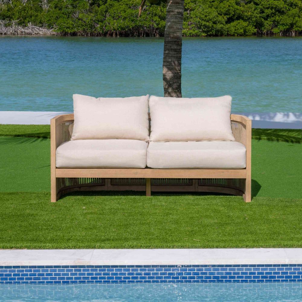 Wooden outdoor sofa with white cushions by a pool and greenery