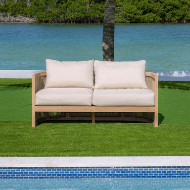 Wooden outdoor sofa with white cushions by a pool and greenery