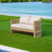 Wooden outdoor sofa with white cushions on a grassy area by a body of water.