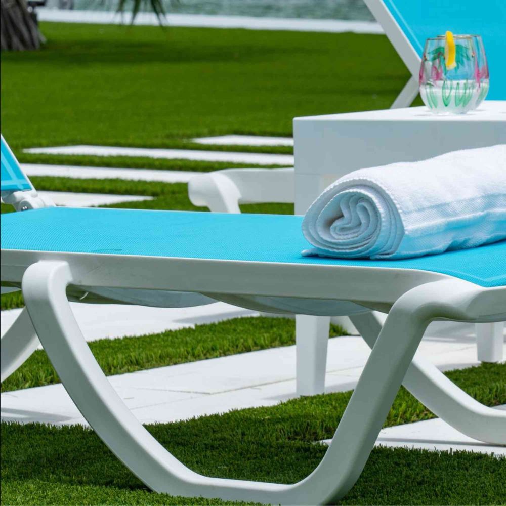 Blue lounge chair with a rolled towel on a grassy area