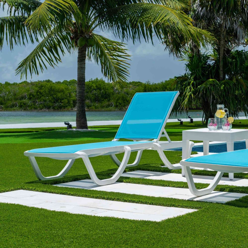 Blue lounge chairs on a grassy area with palm trees and a lake in the background
