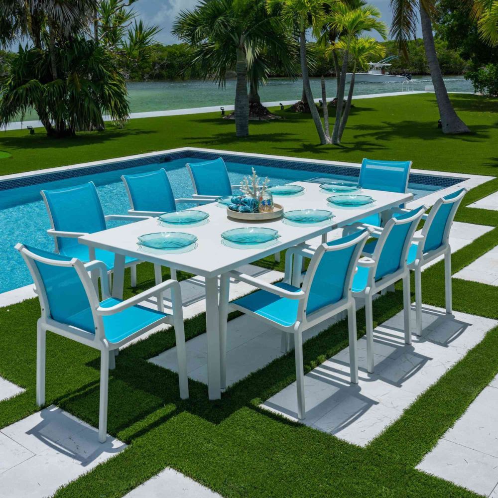 Outdoor dining set with blue chairs and a white table by a poolside.