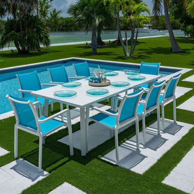 Outdoor dining set with blue chairs and a white table by a poolside.