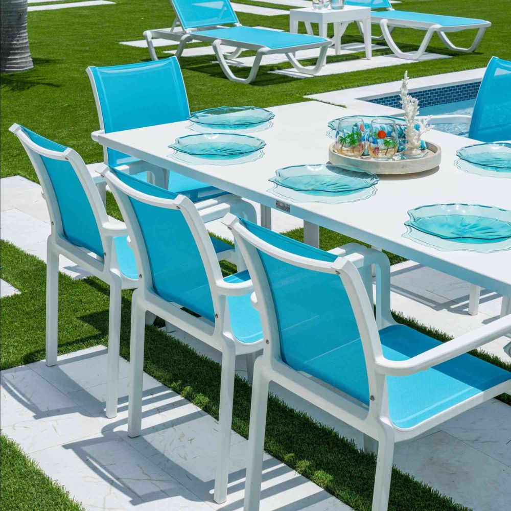 Outdoor dining setup with blue chairs and white table on a grassy area.