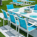 Outdoor dining setup with blue chairs and white table on a grassy area.
