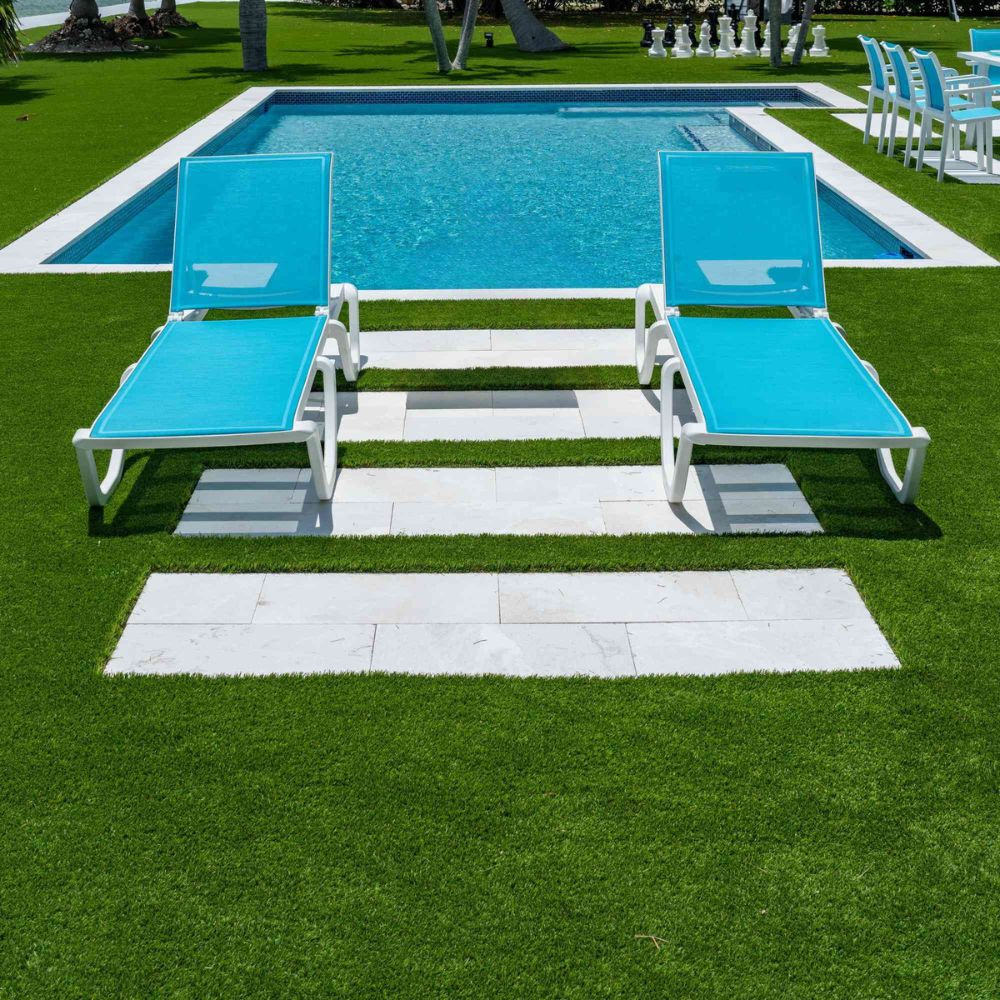 Two blue lounge chairs on a grassy area near a pool.
