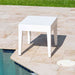 White square table on a patio next to a pool