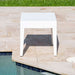 White square table on a stone patio by a pool