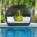 Round wicker outdoor lounge with white cushions by a poolside