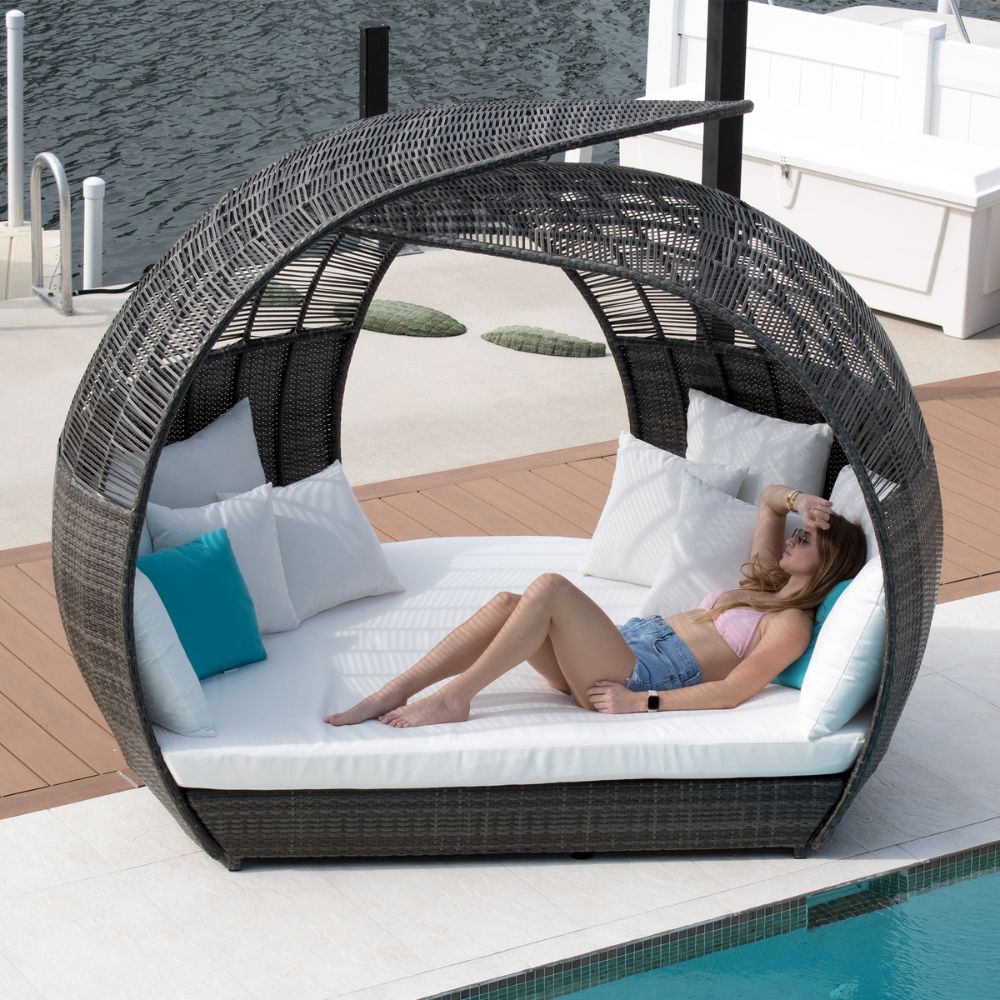 Person relaxing in a circular wicker daybed by a pool