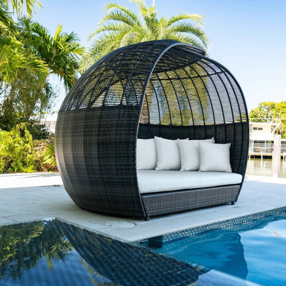 Black woven outdoor chair with white cushions by a poolside