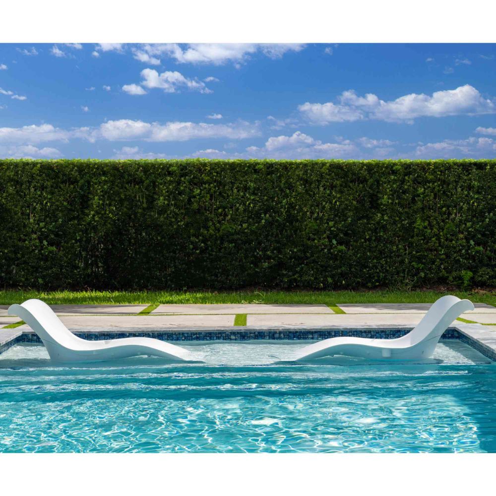 White lounge chair in a pool with a hedge and blue sky background
