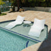 Two white lounge chairs and a small table by a pool with a waterfront view.