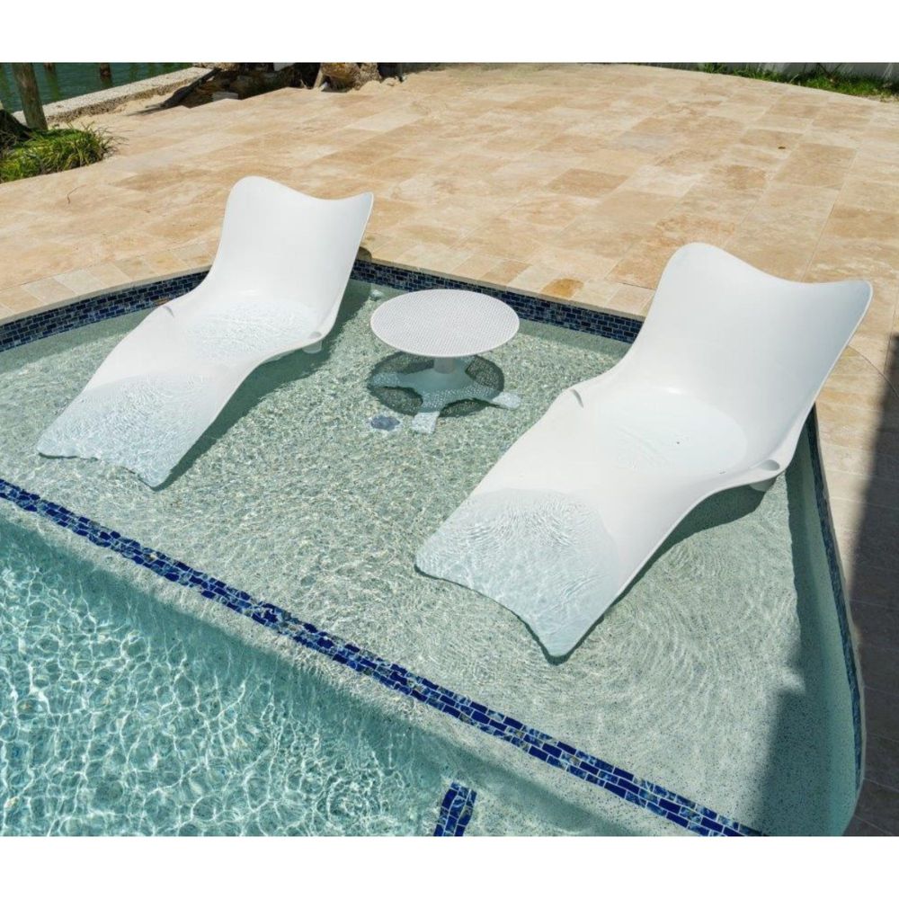 Two white lounge chairs and a small round table by a poolside.
