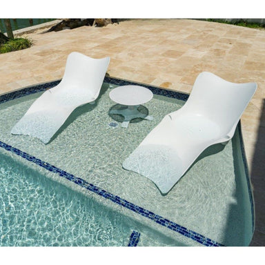 Two white lounge chairs and a small round table by a poolside.