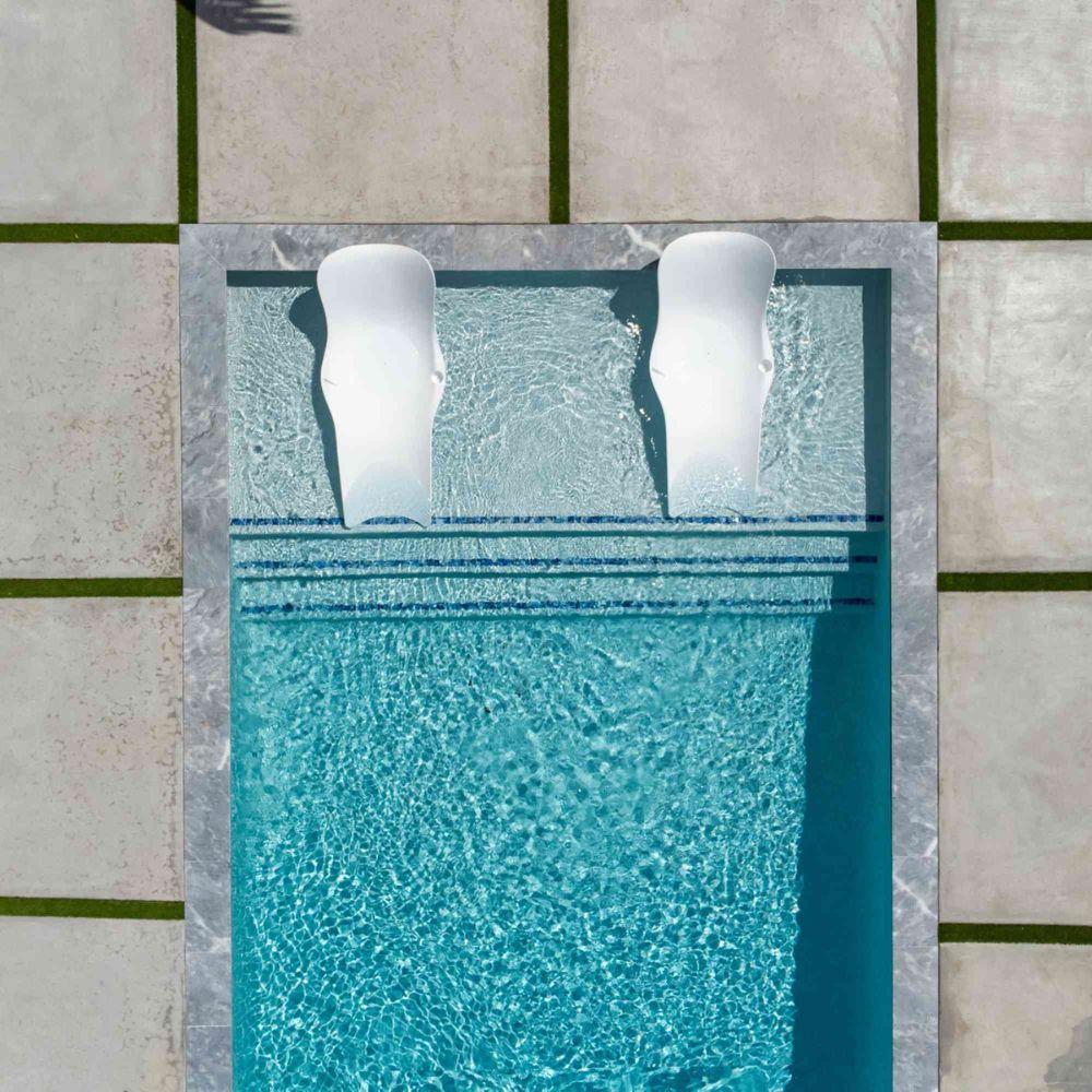 Two white lounge chairs floating in a pool with tiled deck.
