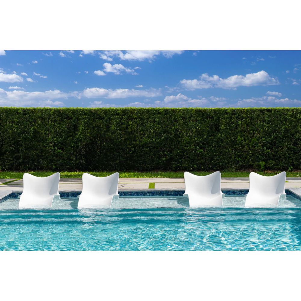 Four white lounge chairs in a pool with a hedge and blue sky in the background