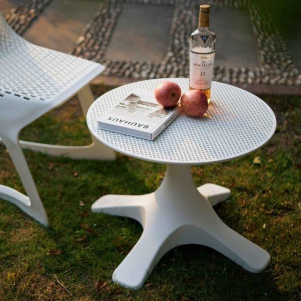 White outdoor table with a bottle of whiskey, apples, and a book on a grassy patio.