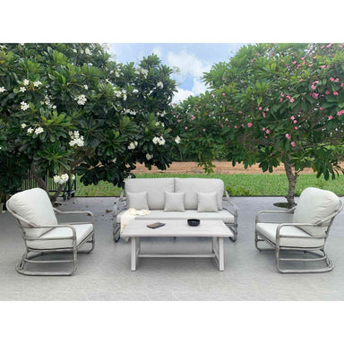 Outdoor patio set with white cushions on a wooden deck surrounded by greenery.
