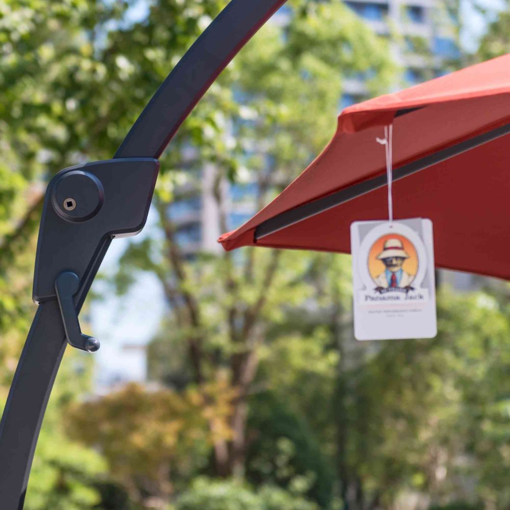 Red outdoor umbrella with a hanging air freshener tag against a blurred green background