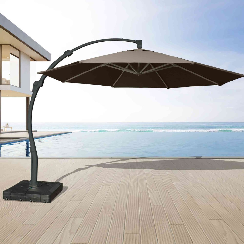 Beige patio umbrella with black stand on a wooden deck by a pool and ocean view.