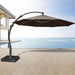 Beige patio umbrella with black stand on a wooden deck by a pool and ocean view.