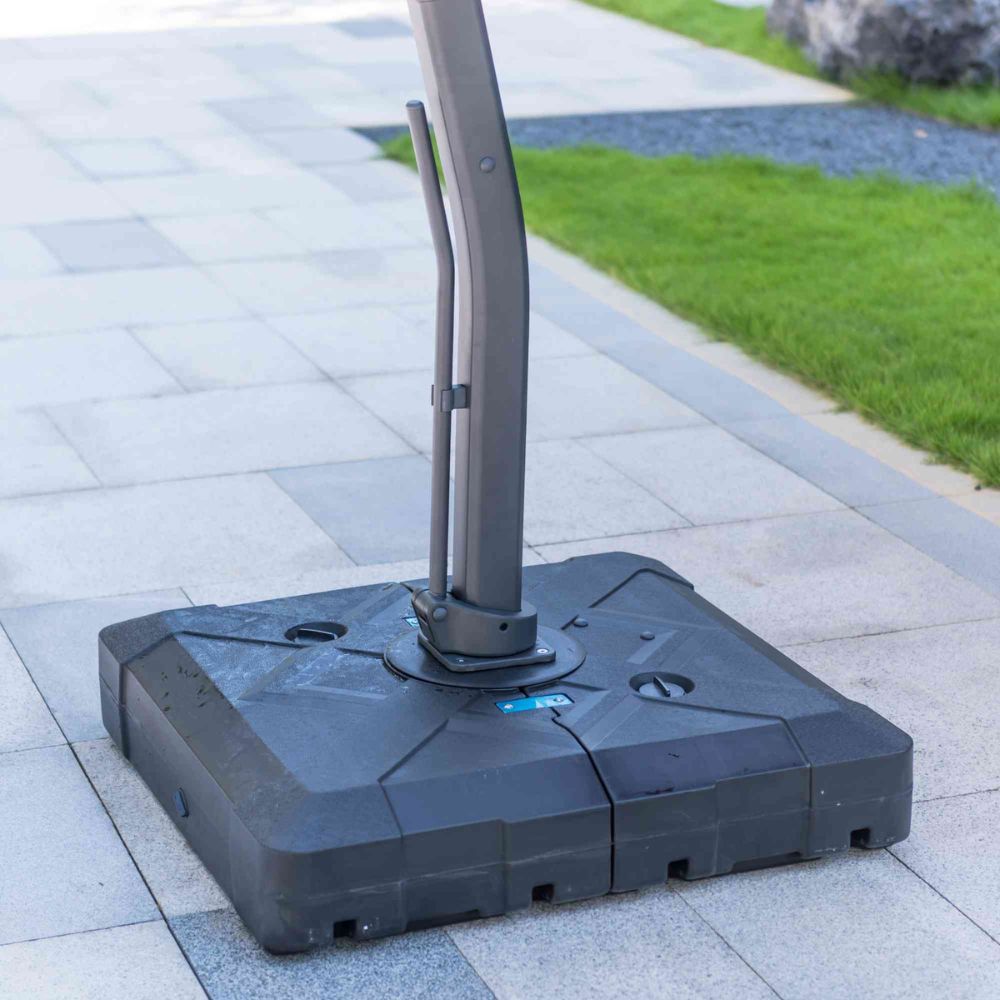 Black patio umbrella base on a paved surface with grass in the background