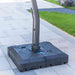 Black patio umbrella base on a paved surface with grass in the background