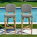 Two bar stools with striped backs and woven seats by a poolside.
