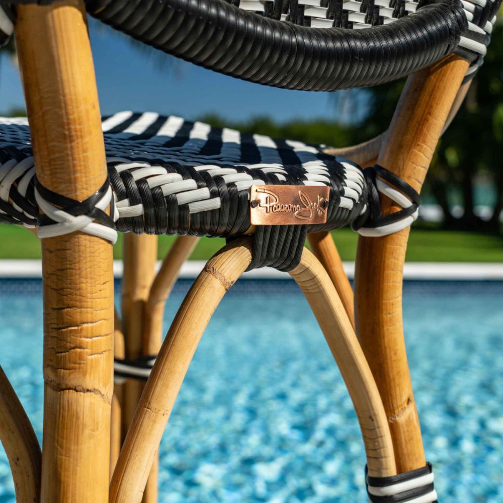 Close-up of a wicker chair with black and white striped cushion by a pool.