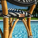 Close-up of a wicker chair with black and white striped cushion by a pool.