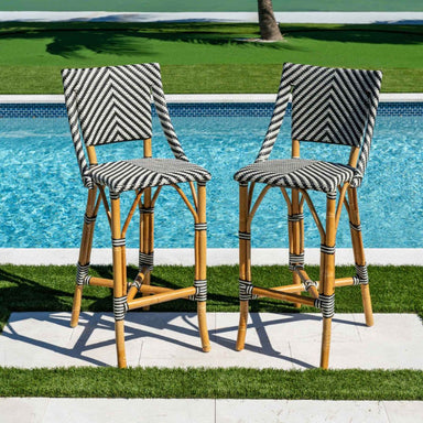 Two striped bar stools by a poolside with green grass and a palm tree in the background.