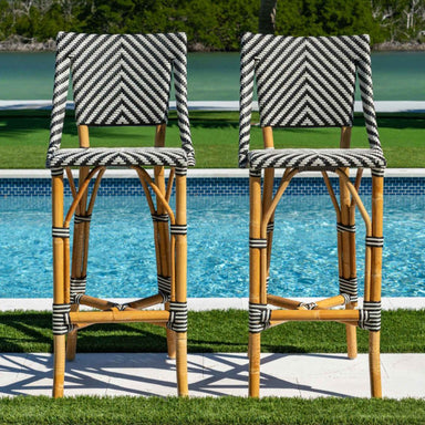 Two striped bar stools with a wicker design in front of a pool.