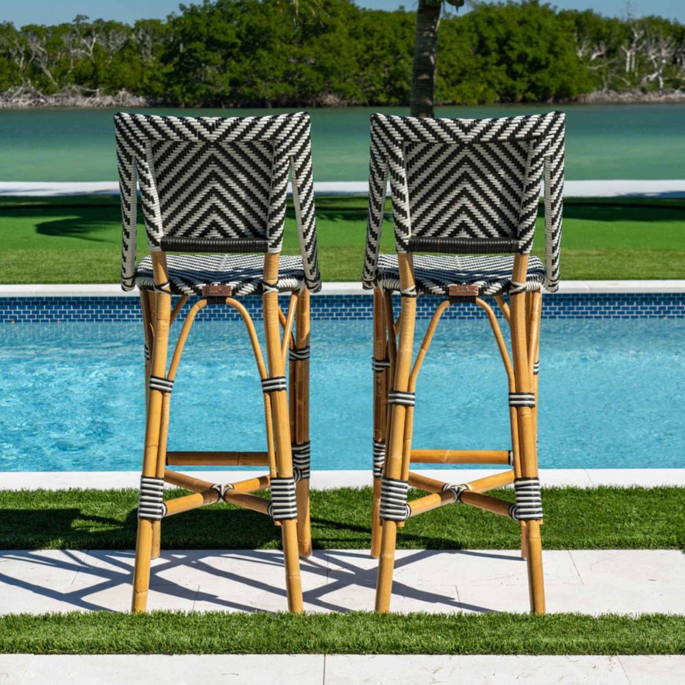 Two patterned bar stools by a poolside with greenery in the background