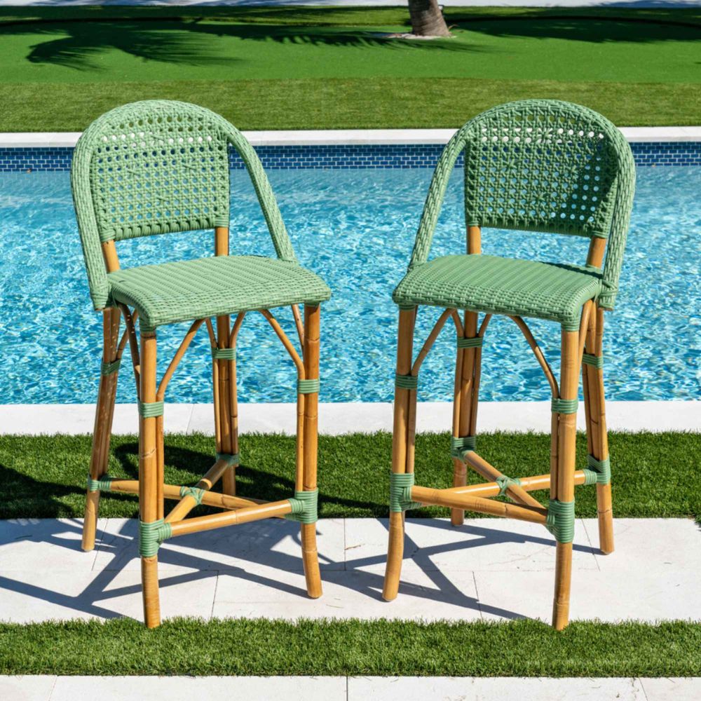 Two green and brown wicker bar stools by a poolside.