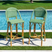Two green and brown wicker bar stools by a poolside.