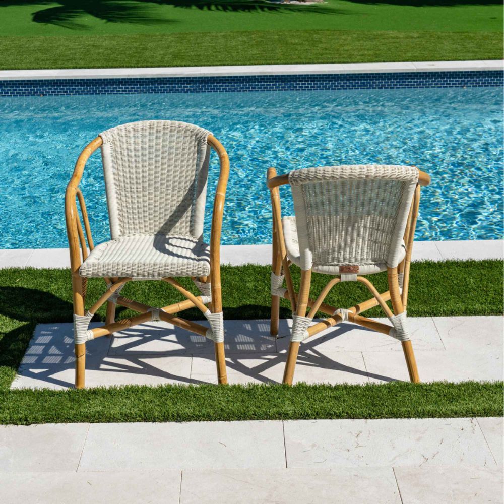 Two wicker chairs with white cushions by a poolside.