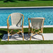 Two wicker chairs with white cushions by a poolside.