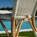 Close-up of a wicker chair with wooden legs by a poolside.