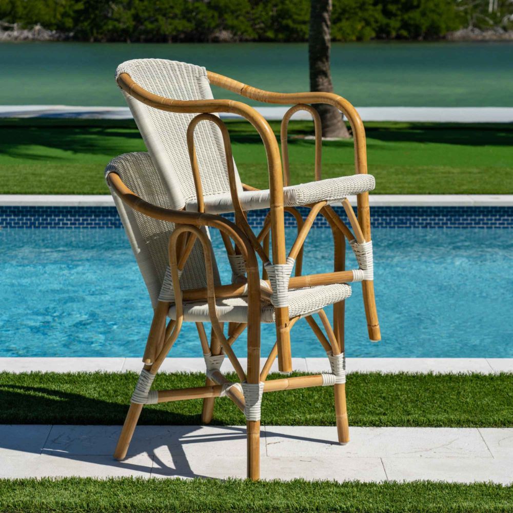 Two wicker chairs with white cushions by a poolside