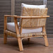 Bamboo armchair with woven backrest and white cushions on a wooden floor.