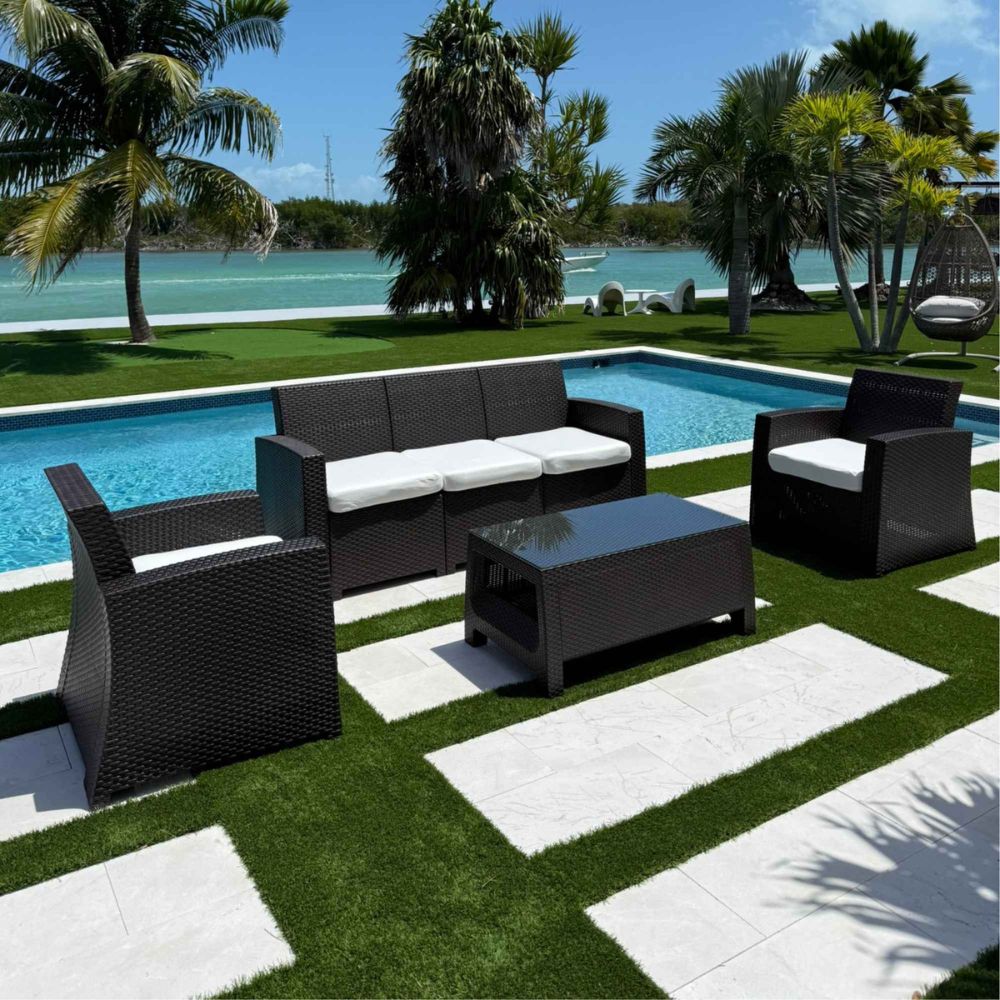 Outdoor patio set with black furniture by a poolside with palm trees in the background.