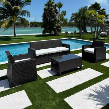 Outdoor patio set with black furniture by a poolside with palm trees in the background.