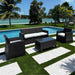 Outdoor patio set with black furniture by a poolside with palm trees in the background.