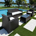 Outdoor patio furniture set with black wicker chairs and table on a grassy area near a pool.