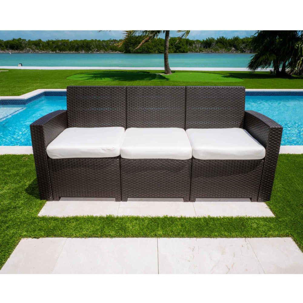 Outdoor wicker sofa with white cushions by a poolside