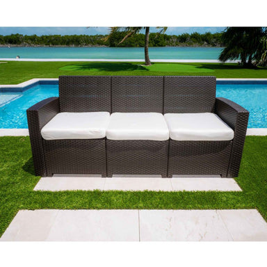 Outdoor wicker sofa with white cushions by a poolside