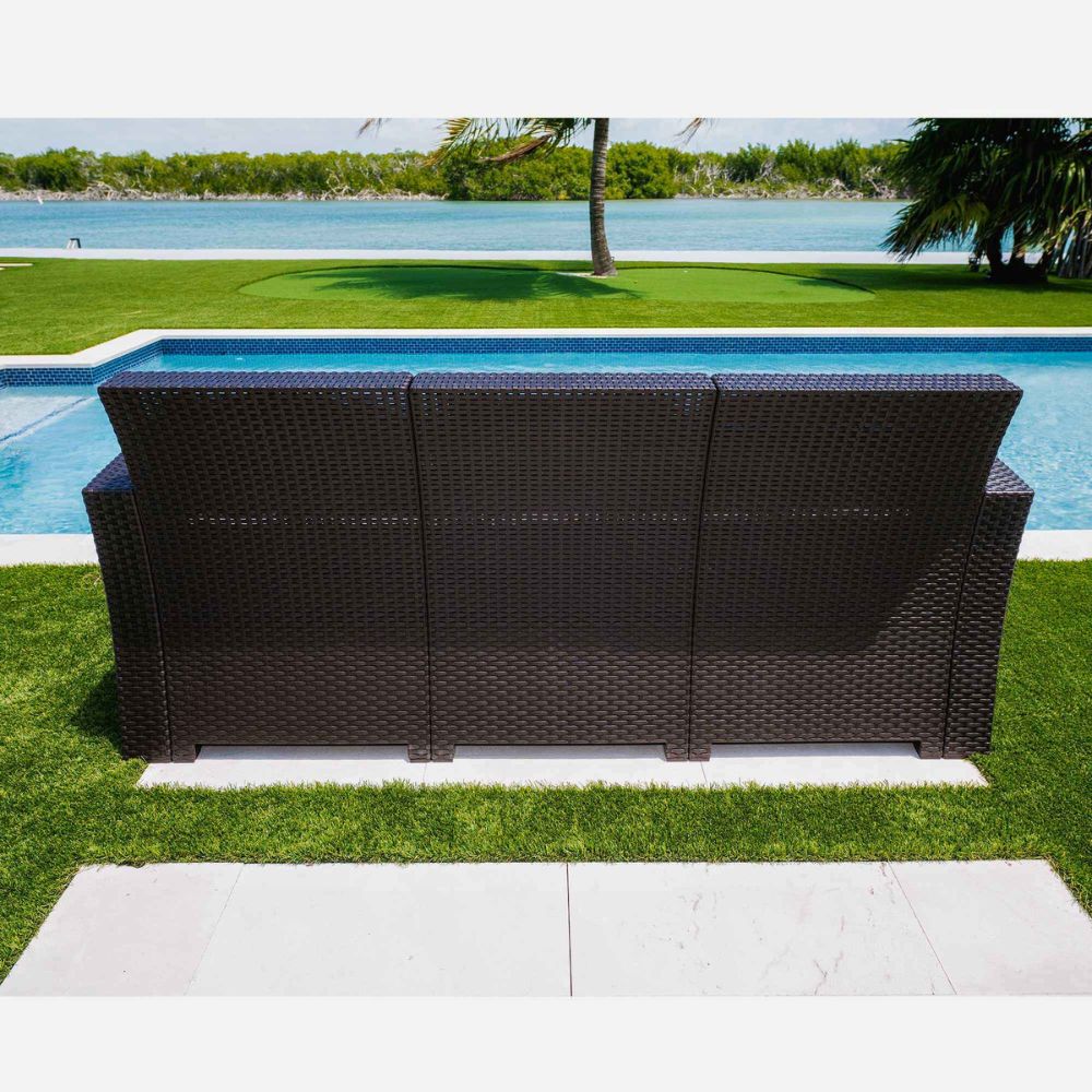 Brown wicker outdoor sofa on a patio with a pool and greenery in the background