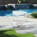 White chair by a pool with green grass and plants in the background