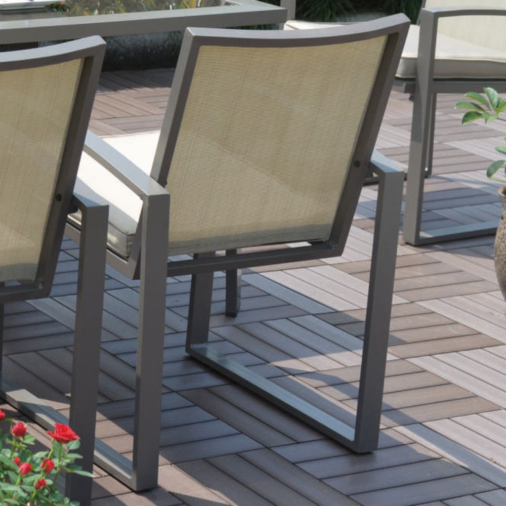 Beige outdoor chairs on a wooden deck with a potted plant and flowers in the foreground.